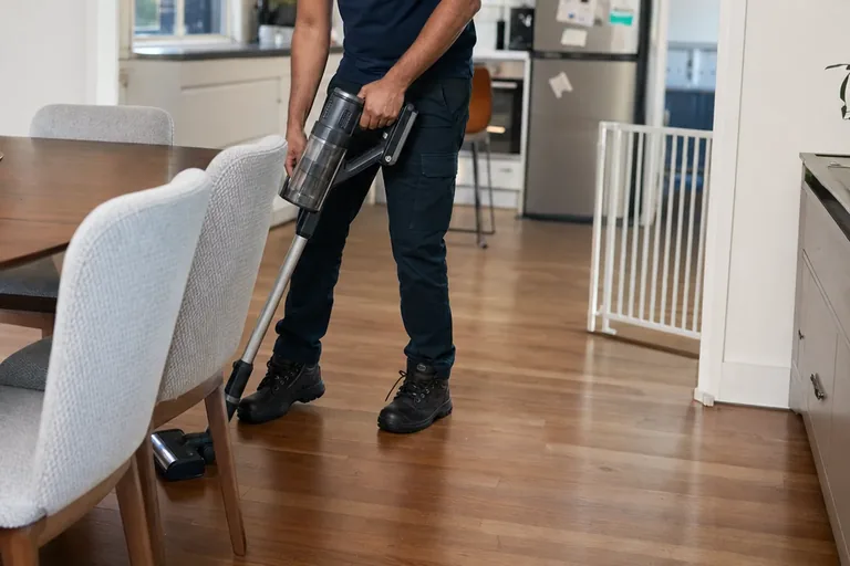 Professional cleaner vacuuming around furniture during a detailed home clean