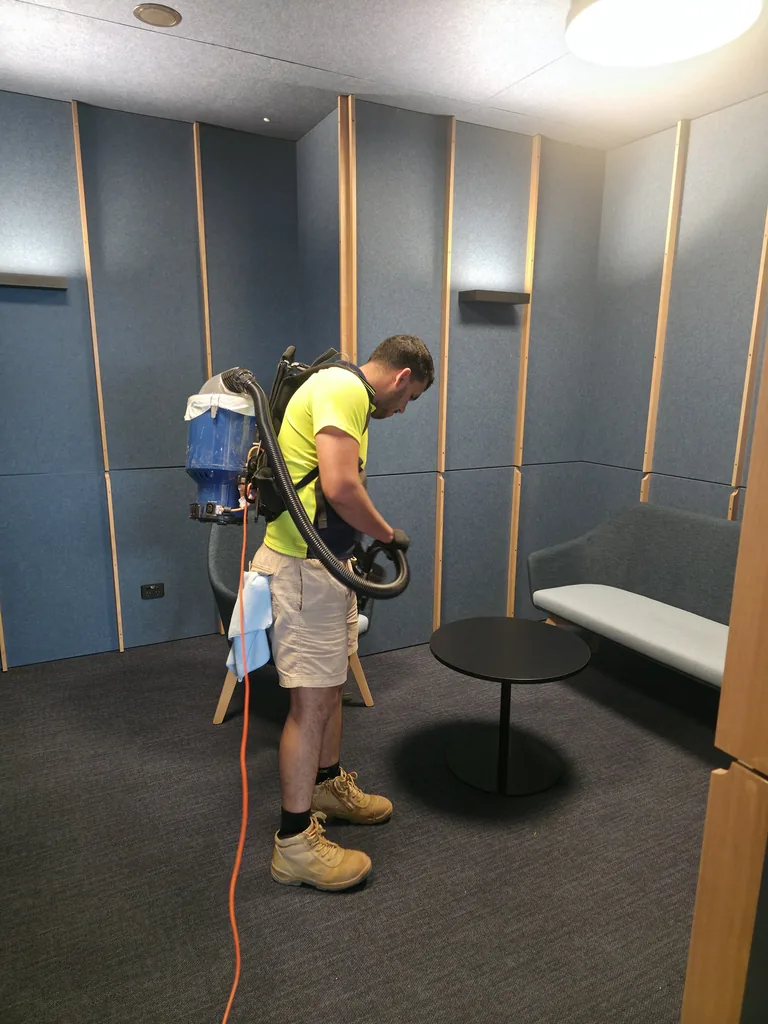 Tas Clean cleaner vacuuming the carpet in a meeting area