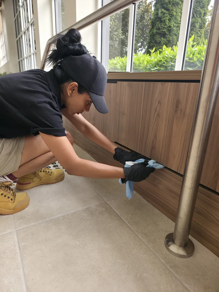 Cleaner wearing gloves hand detailing timber panels beside the Watergarden stairs