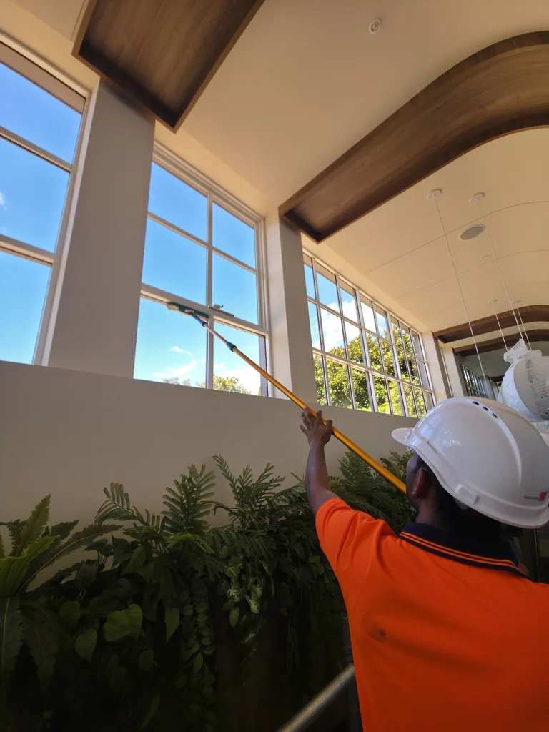 Cleaner in a hard hat and orange hi-vis using an extension pole on the high Watergarden windows
